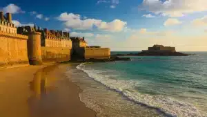 Vue panoramique des remparts de Saint-Malo entourés par la mer à marée haute avec la plage de sable fin au premier plan