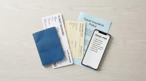 Vue de dessus de documents de voyage : passeport bleu, billets d'avion, carte de vaccination, assurance, et smartphone avec checklist.